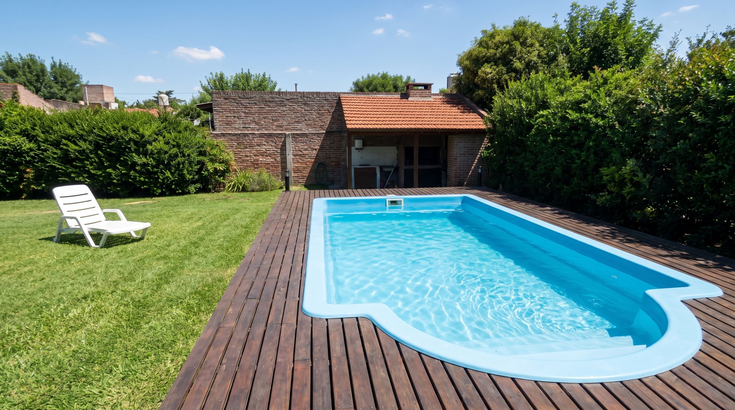 Pileta de fibra celeste con escalera en arco, en un deck de madera de un patio con césped