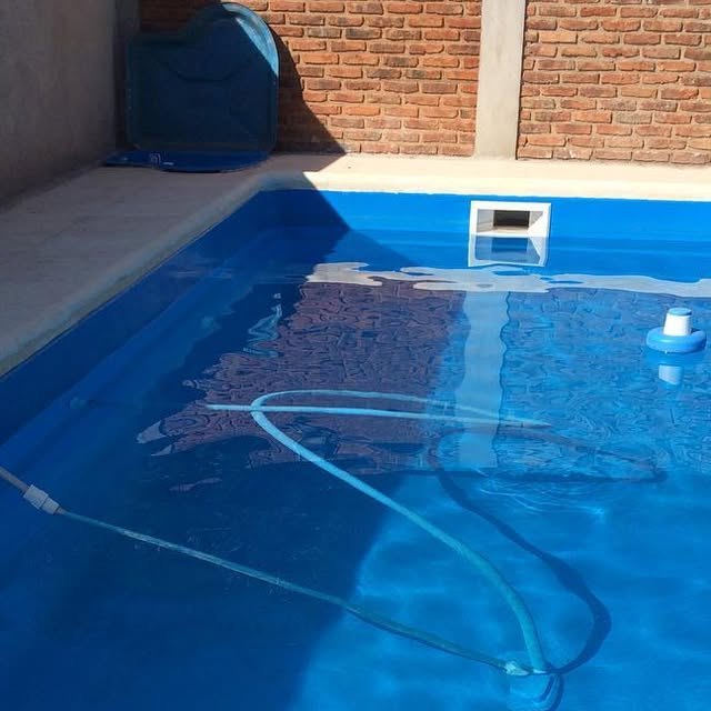 Pileta de fibra celeste con agua en un patio con paredes de ladrillo